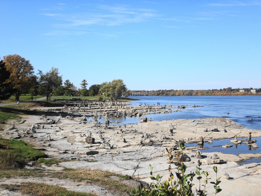 Under a beautiful, blue sky, balanced stone sculptures crowd the exposed shoreline rocks at Remic Rapids.
