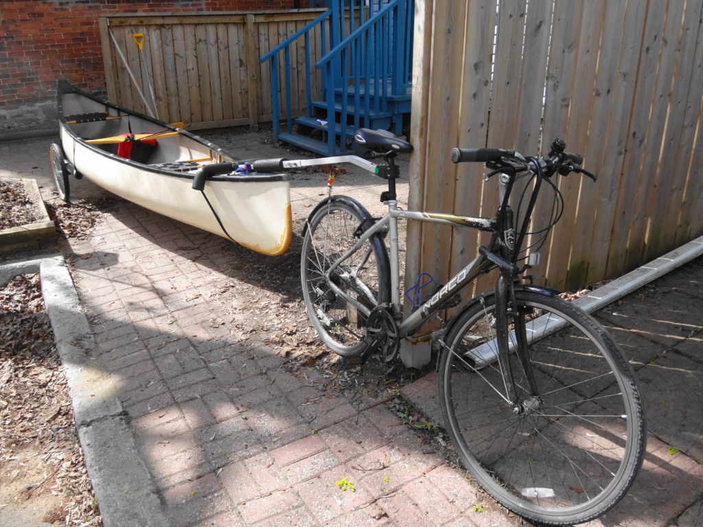 A canoe rides on a trailer attached to a bicycle.