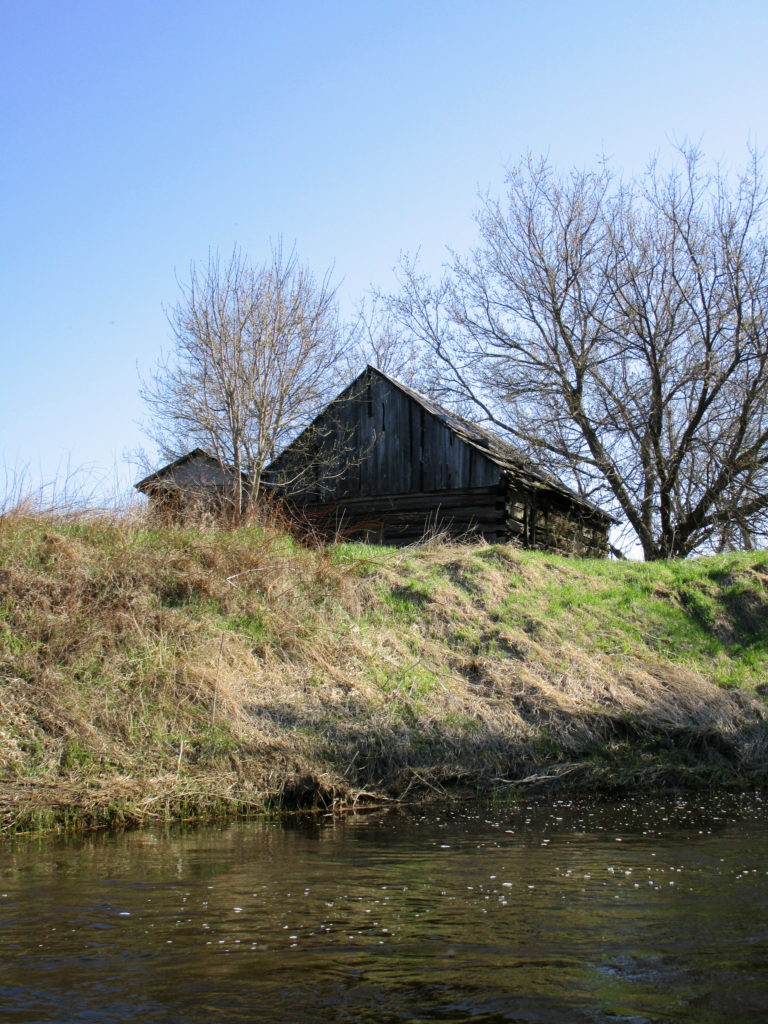 A dilapidated farm building sits on a high bank beside the Jock River.