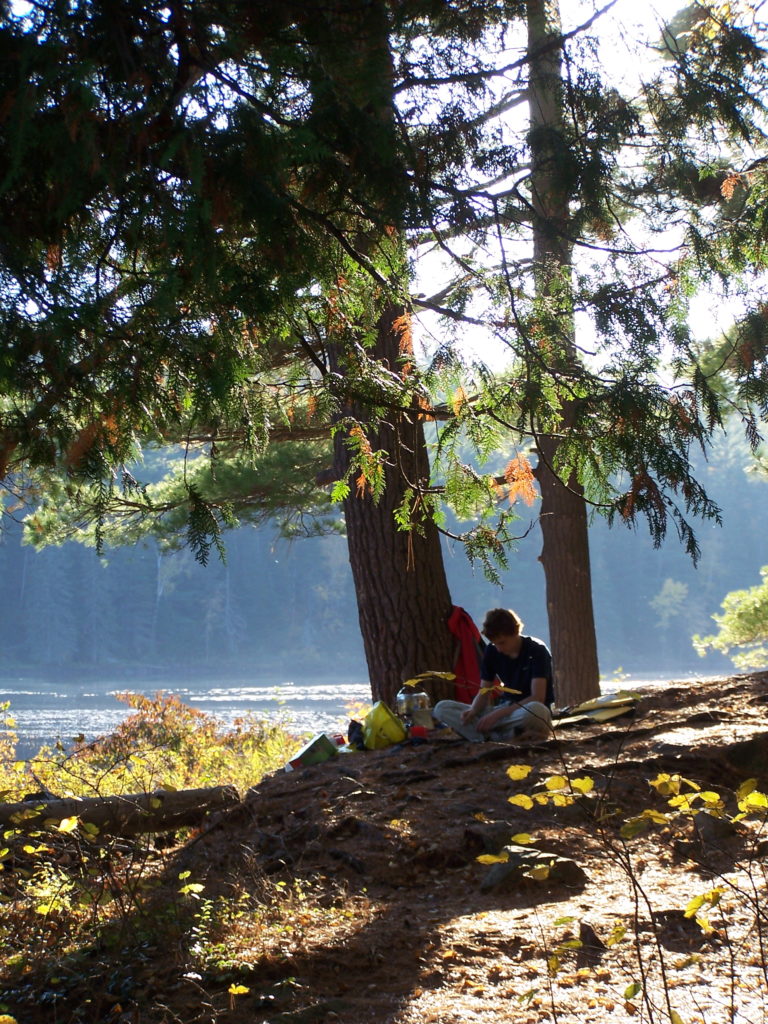 A boy sits under a tree with the Barron River in the background.
