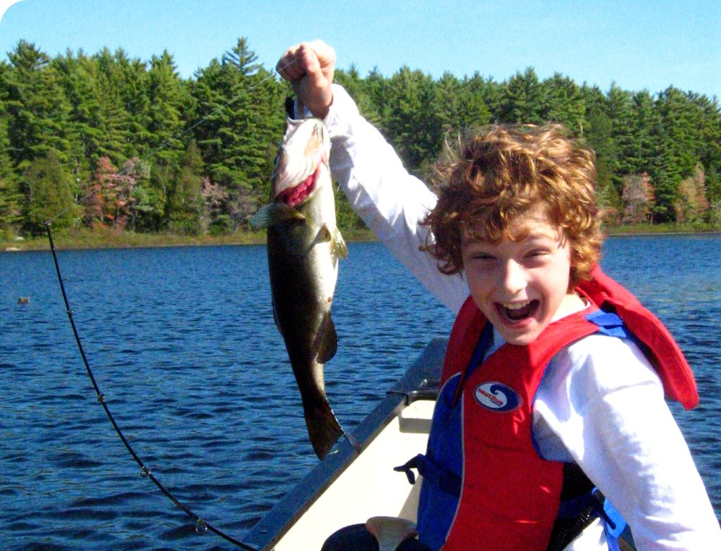 A young boy in a canoe holds up a fat bass.
