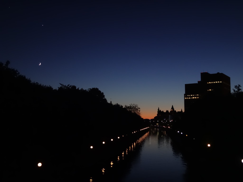 Twilight on the Corkstown Footbridge. A bright planet and crescent moon hang in a dark, navy-blue sky. A faint orange glow lingers behind the distant Gatineau Hills.