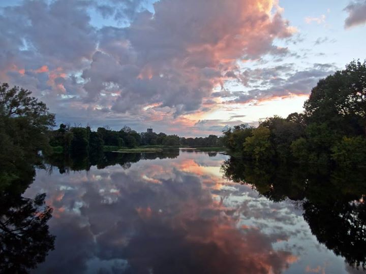 At sunset, glowing clouds reflect in the still water of the Rideau River.