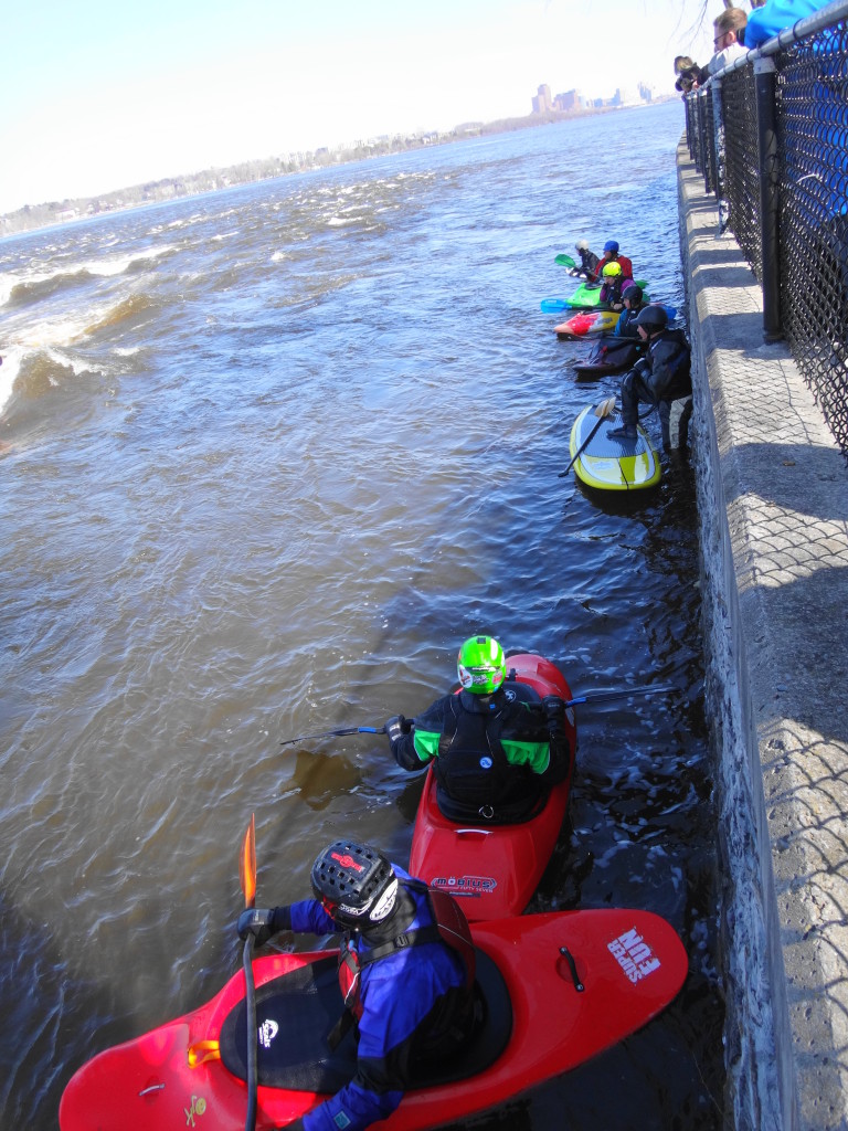 Kayakers and a stand-up paddleboarder float along the shoreline waiting for their turn on "The Wave".