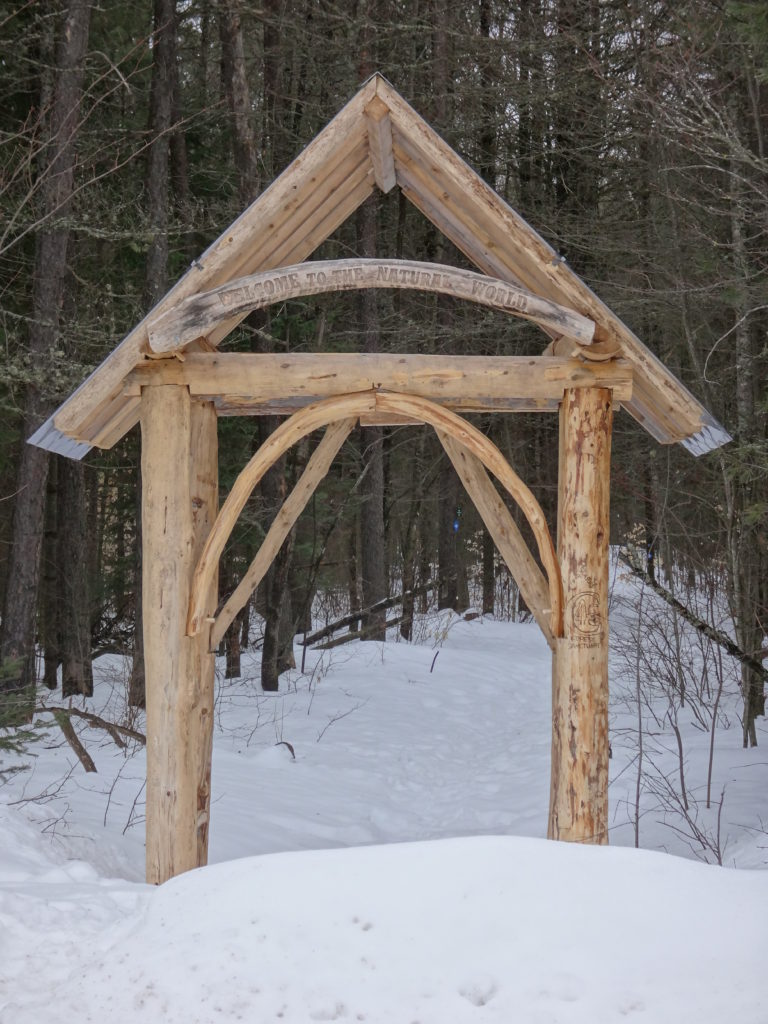 A wooden archway spans an entrance to the Four Seasons Conservation Forest trail network.