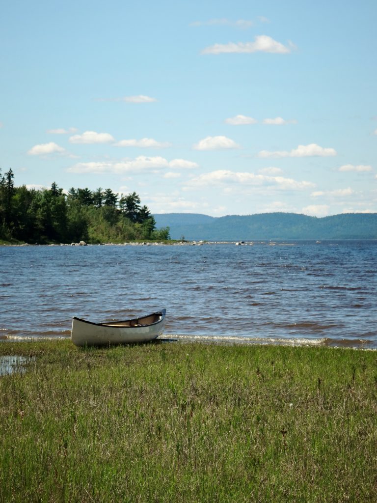 A canoe rests sandy shoreline, with the Ottawa River in the background.