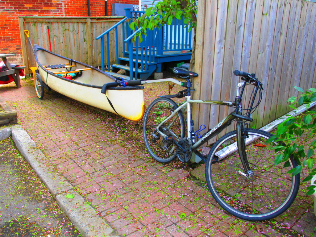 A canoe rests on a towed trailer behind a bicycle.