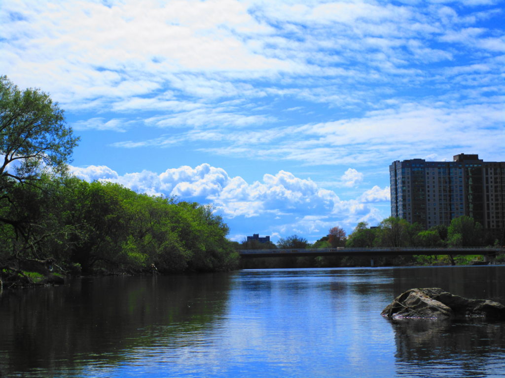A blue sky and fair weather clouds hang over the Rideau River and the Hurdman Transit Bridge.