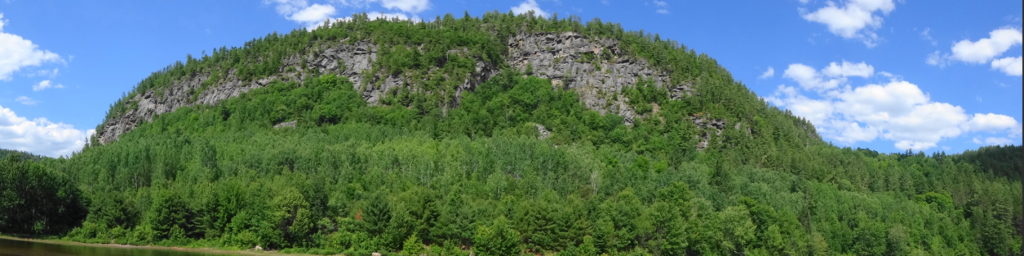 A wide angle photograph shows the towering rock face above Baie de la Presqu'ile d'en Bas.