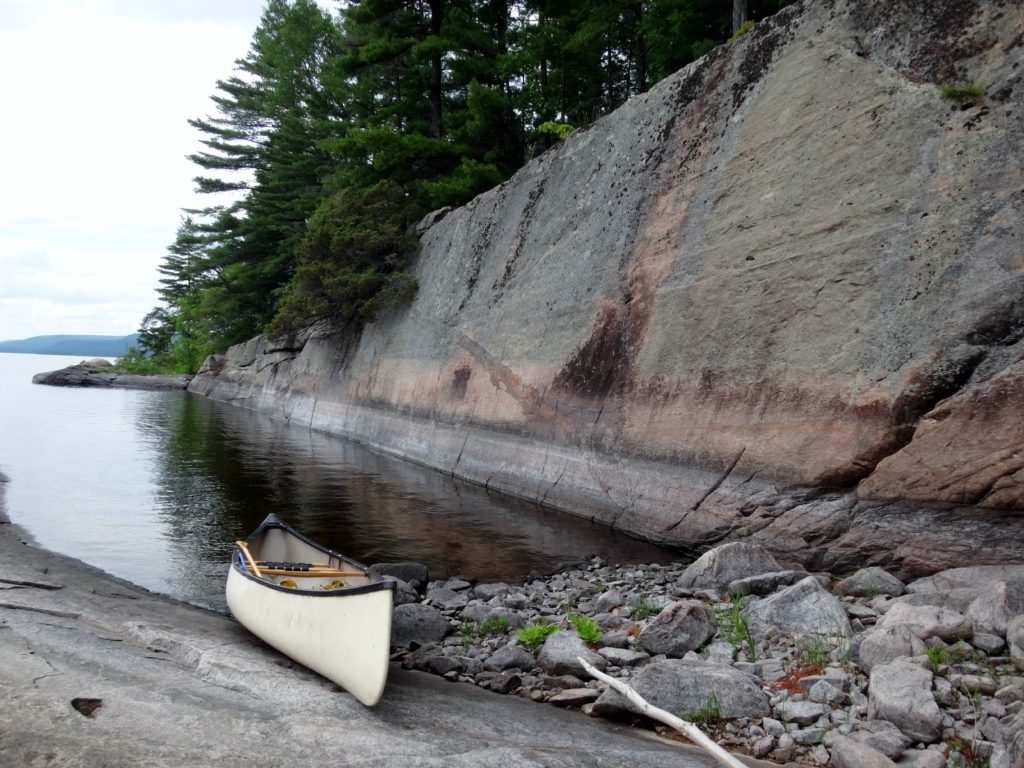 A canoe is pulled up on to a rocky shore beside a long flat wall of stone.