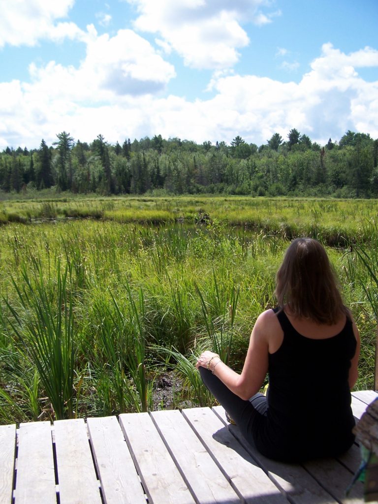 A woman meditates on a deck overlooking a wetland in the Four Seasons Conservation Forest, Deep River