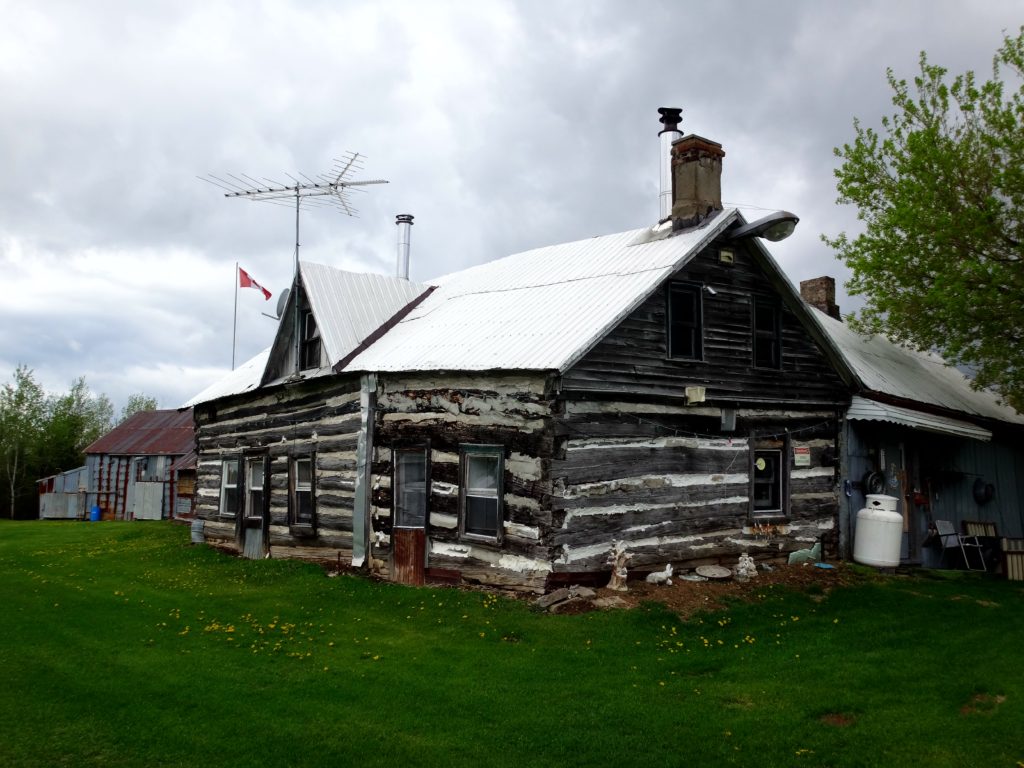 A city-owned, heritage log farmhouse lies under a grey sky on a farm in the Marlborough Forest.